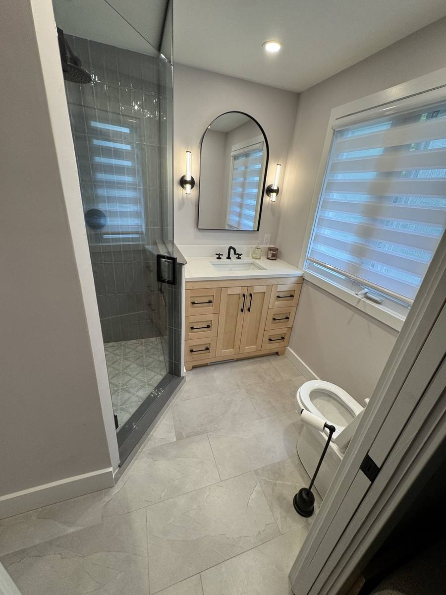 Renovated primary ensuite in Orleans with grey vertical tile shower, glass door and maple vanity